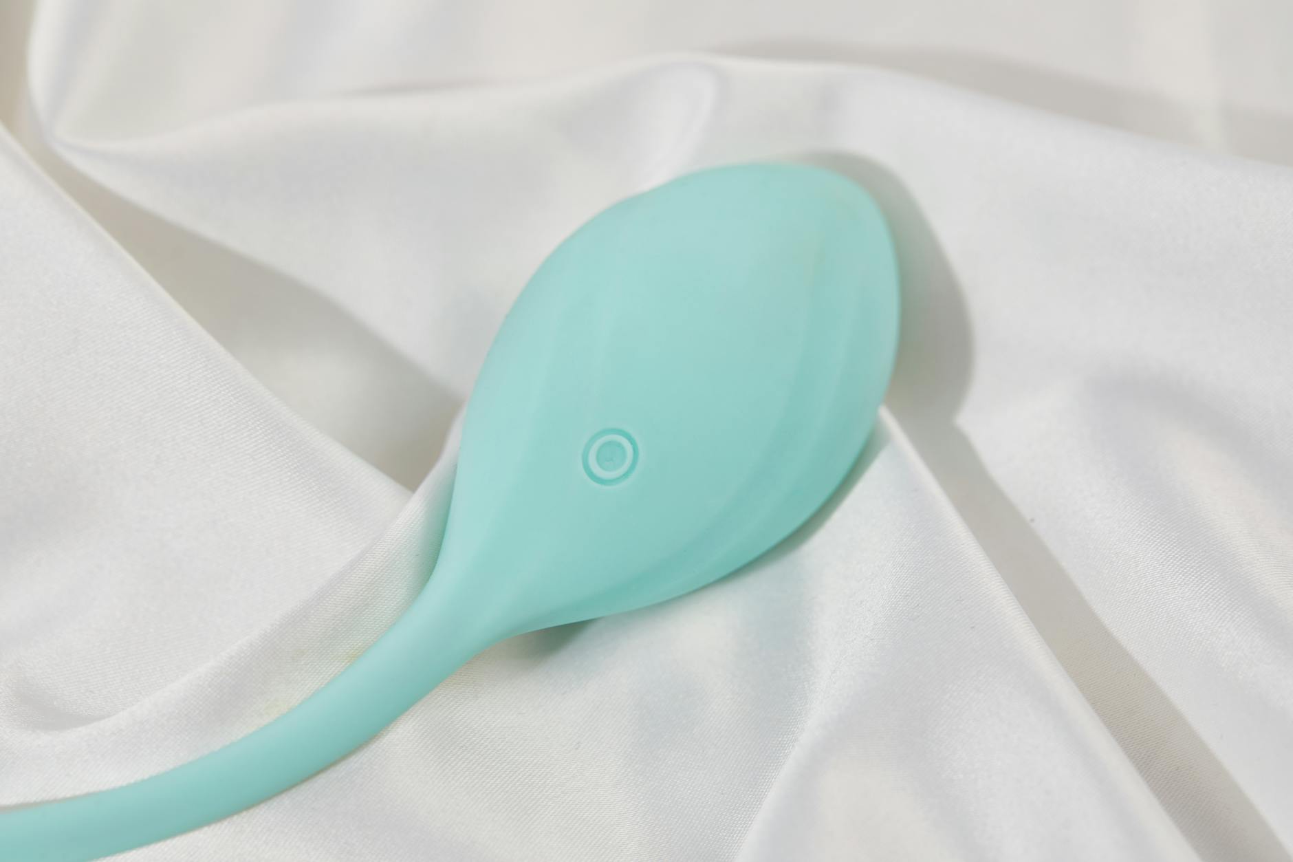 A stylish teal vibrator on smooth white silk fabric, emphasizing comfort and elegance.