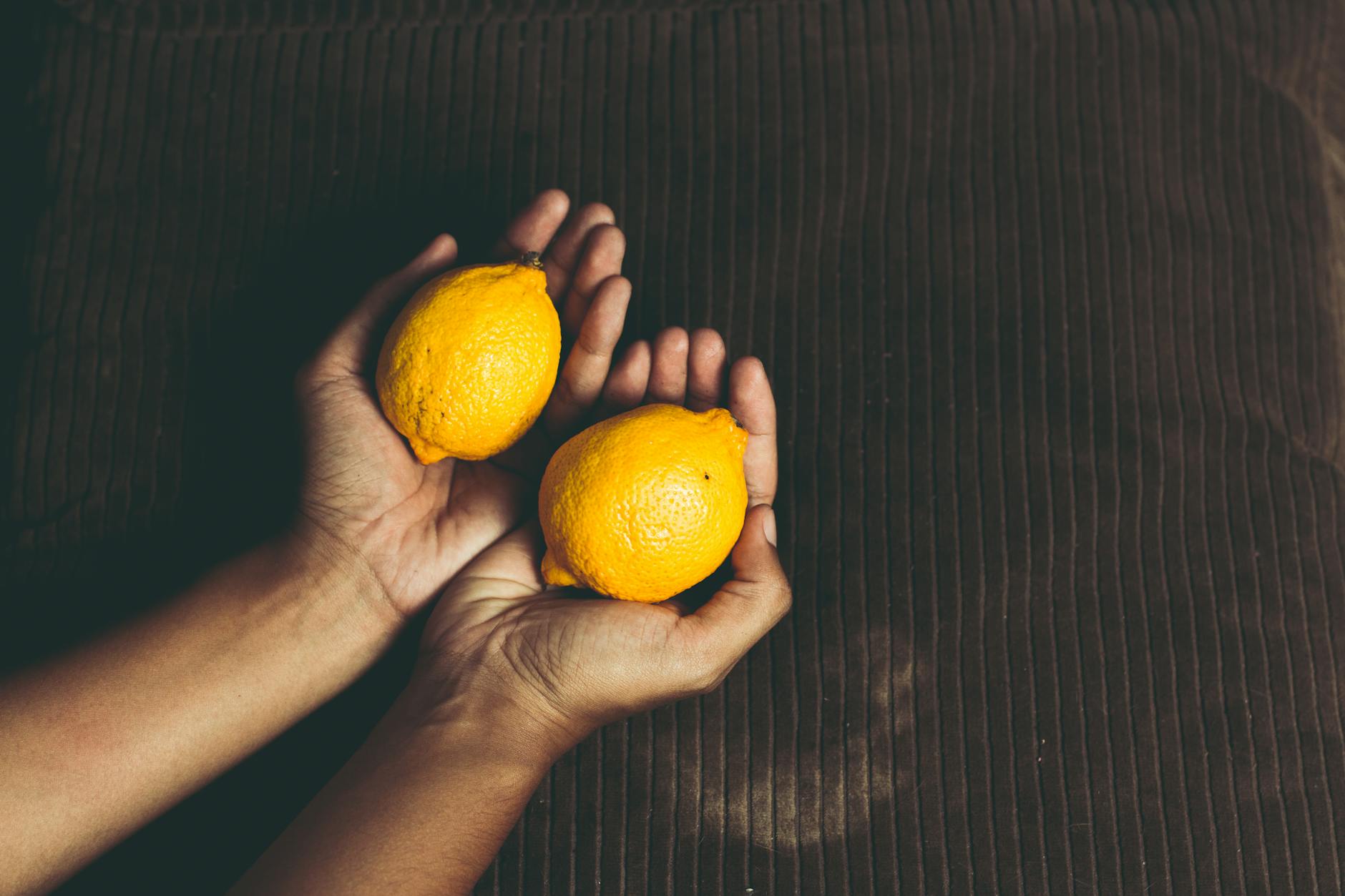 Due limoni freschi tenuti in mano su una superficie marrone, simbolo di freschezza e rinascita