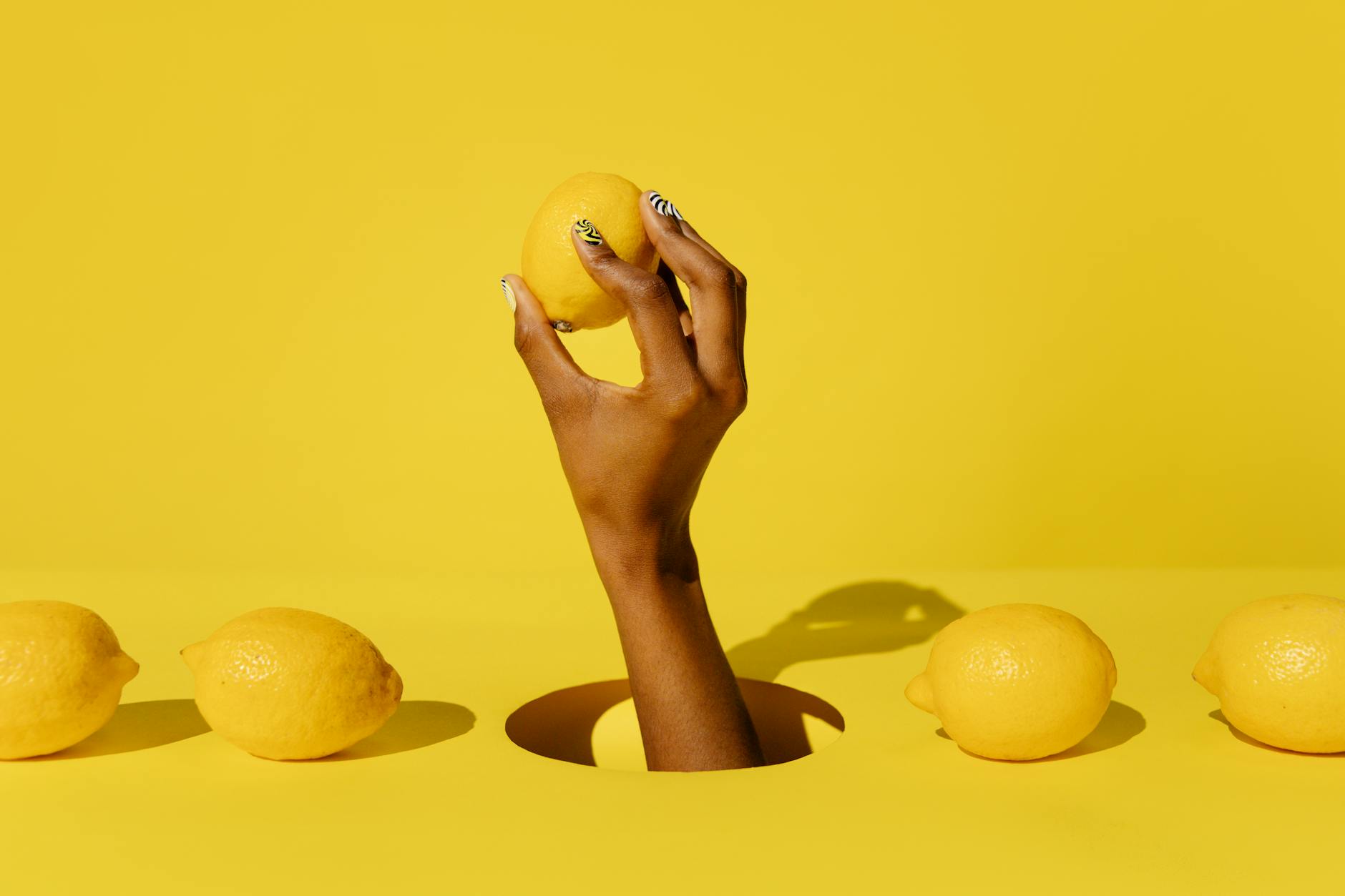 Una mano che tiene un limone contro uno sfondo giallo vivace, trasmettendo un'atmosfera fresca e consapevole