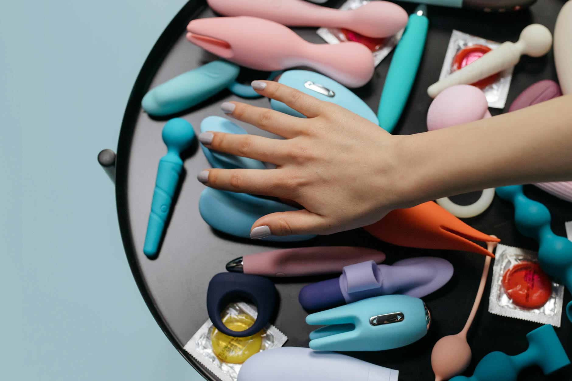 Una mano che raggiunge una varietà di vibratori colorati disposti su un tavolo