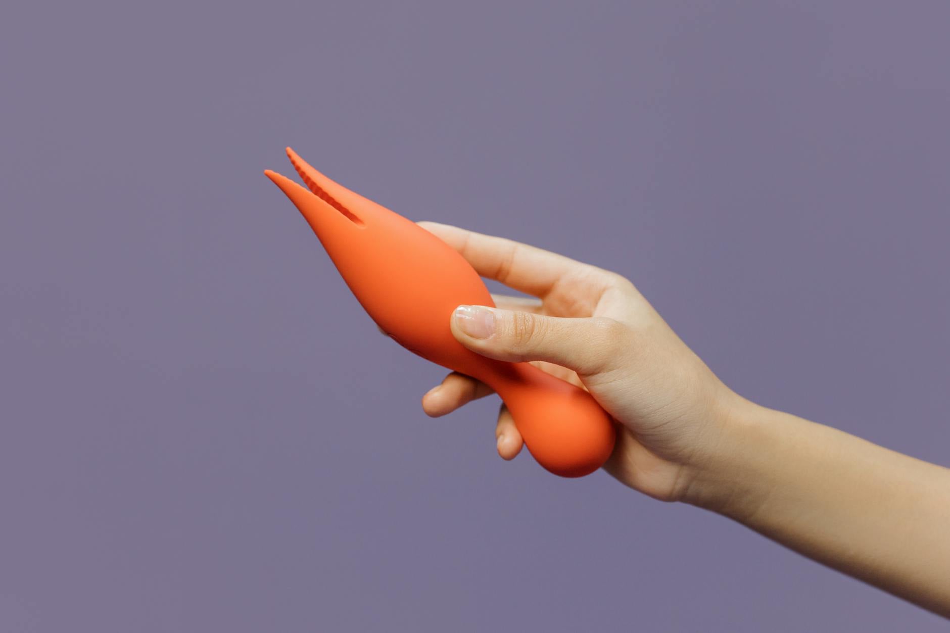 Mano che tiene un vibratore arancione su uno sfondo minimalista viola, con intima sensualità moderna.