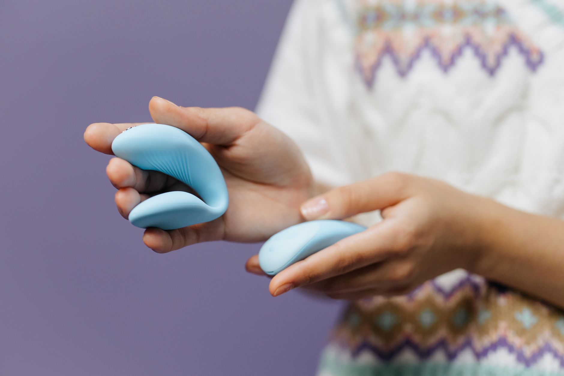 Close-up of hands holding a blue personal massager against a knitted sweater