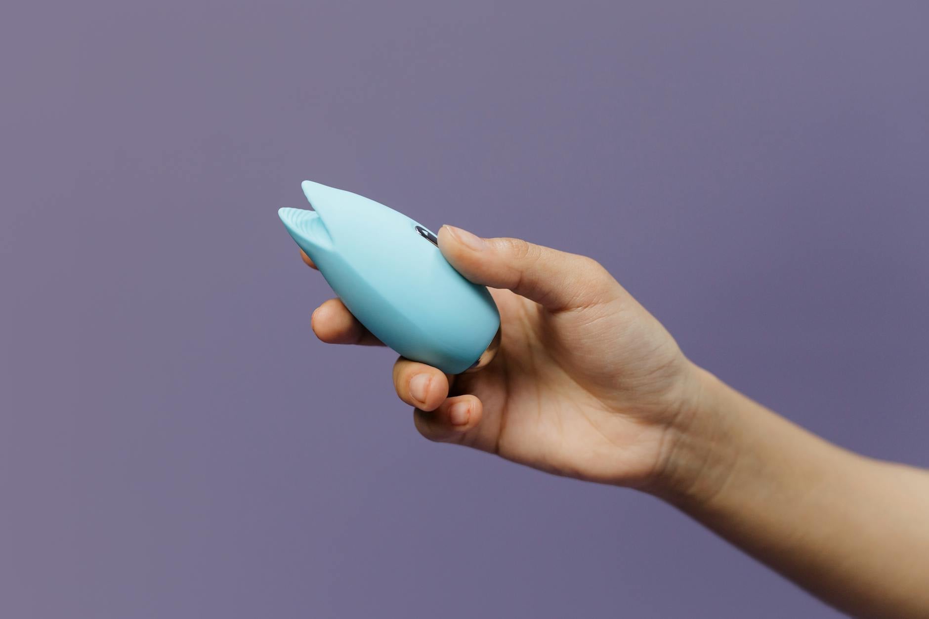 Due mani che reggono vibratori in silicone rosa e blu su sfondo pastello