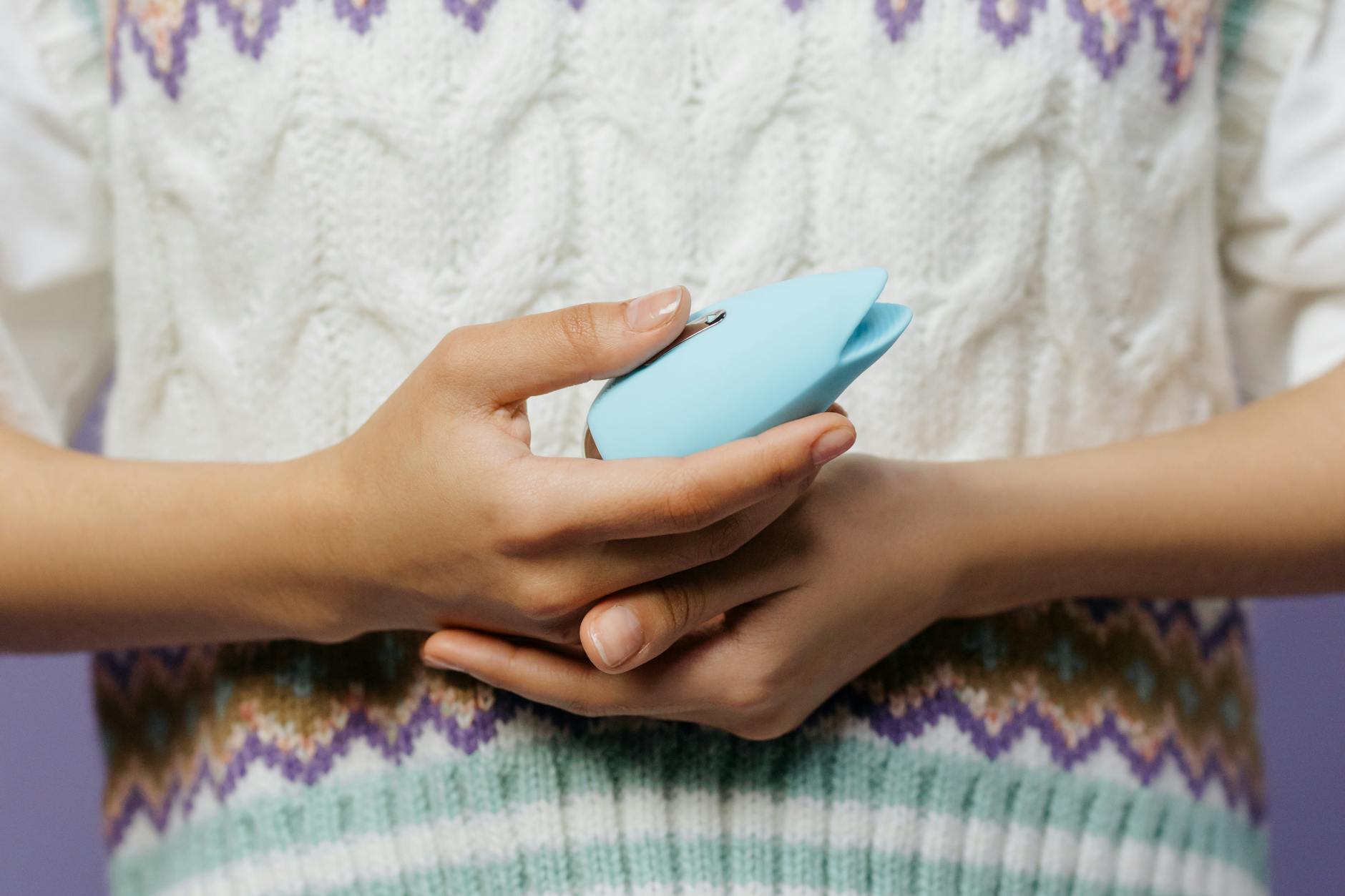 Primo piano delle mani che tengono un massaggiatore personale blu contro un maglione a maglia