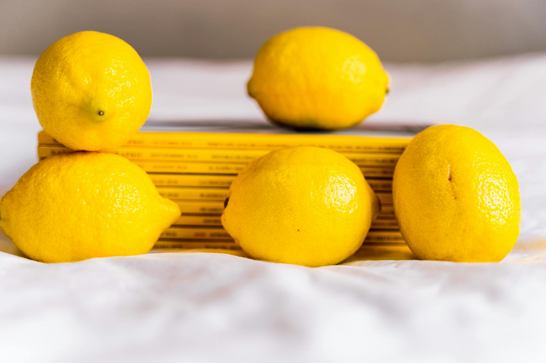 Mano con unghie bianche che tiene un limone su sfondo rosa morbido, circondata da altri limoni